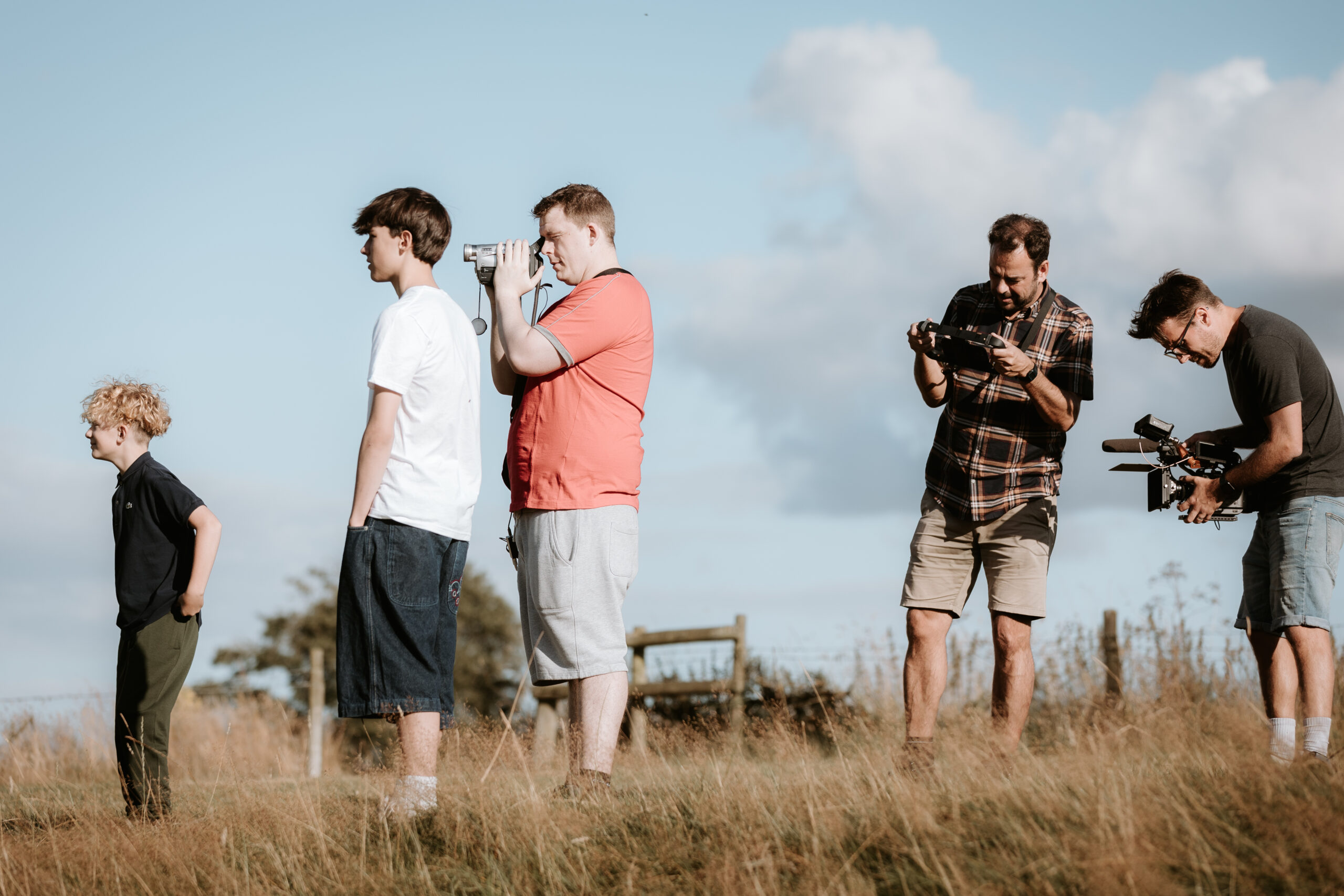 A group of 3 men and 2 young boys with camera equipment. In long grass