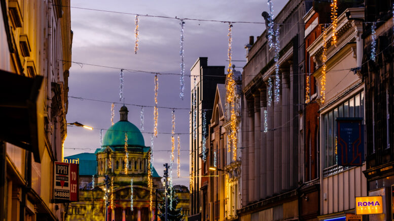 Christmas lights hanging across a shopping street at dusk with buildings in the background