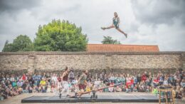 A crowd watch as a person is launched into the air from a seesaw on the ground