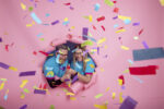 two people in blue volunteer tshirts bursting through a pink wall with a large confetti cannon