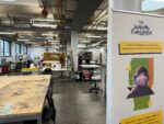 A picture of a large room with tables and chairs and a pull up poster advertising Makerspace