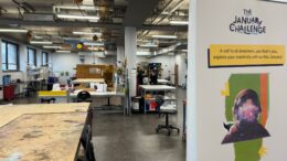 A picture of a large room with tables and chairs and a pull up poster advertising Makerspace