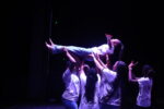 A group of young dancers in white tshirts hold another dancer in the air