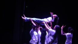 A group of young dancers in white tshirts hold another dancer in the air