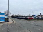 A road with 2 junctions at either side of the image and carpark behind the road.