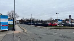 A road with 2 junctions at either side of the image and carpark behind the road.