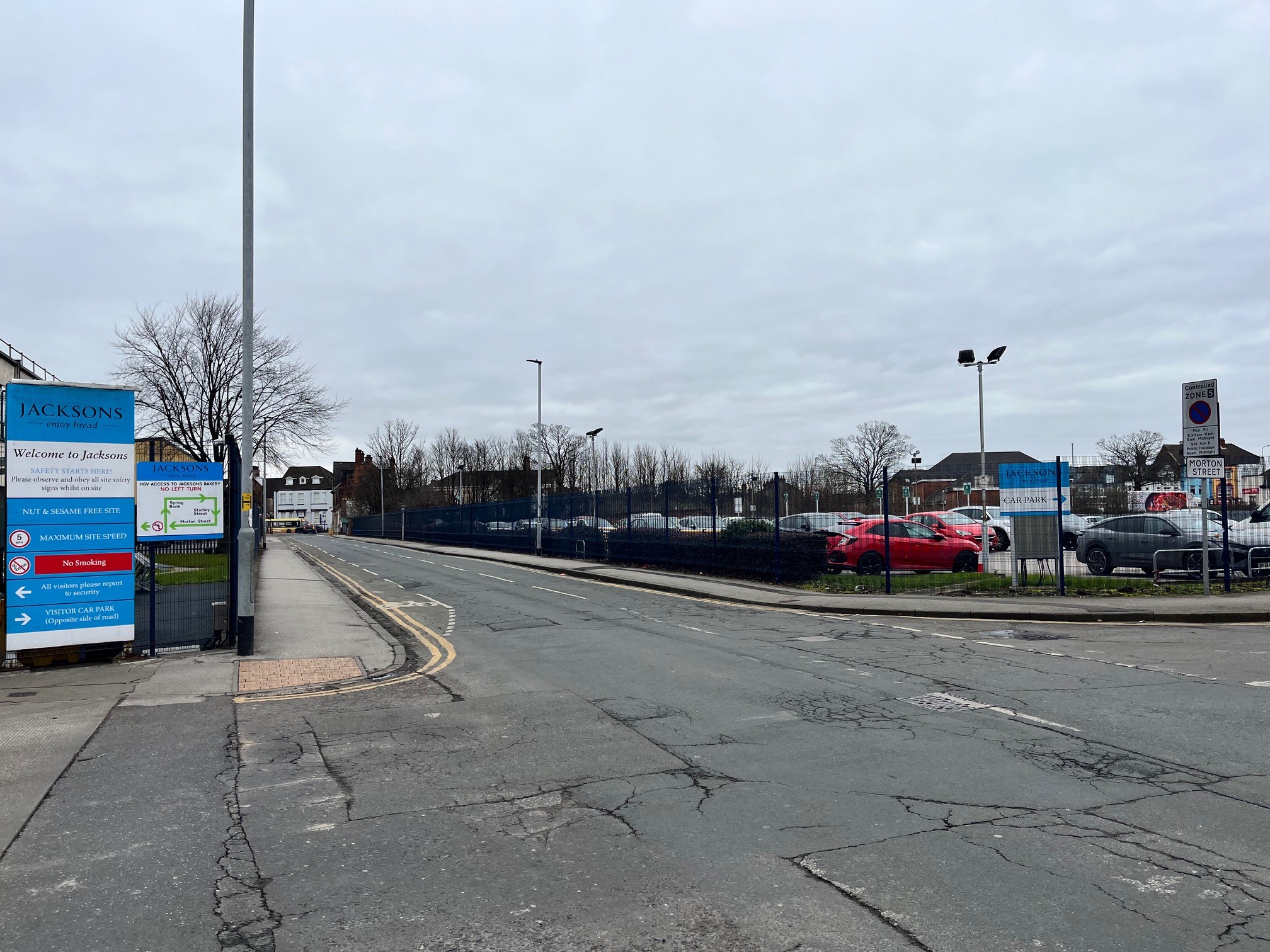 A road with 2 junctions at either side of the image and carpark behind the road.