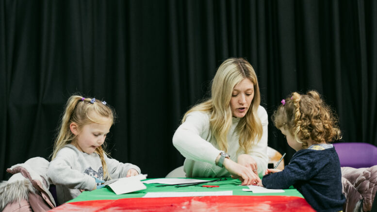 an adult and two children sit at a table doing crafts together