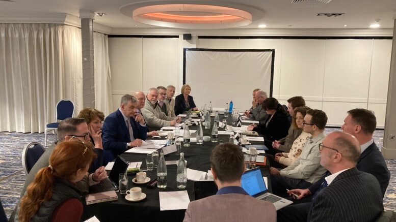 A large group of people sit around a meeting table