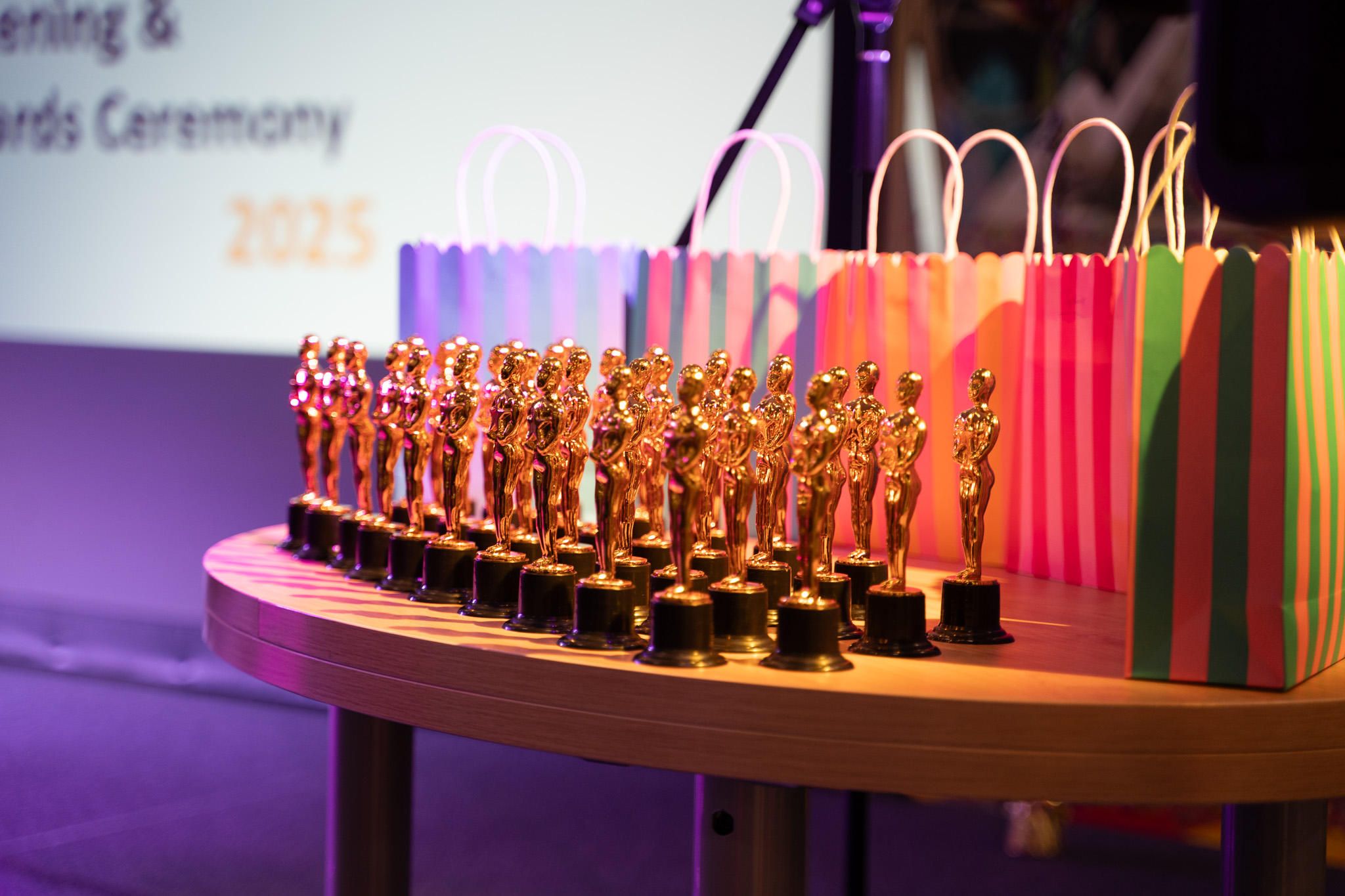 A close up on a table with a number of small gold Oscar-style trophies on a table with a screen in the background