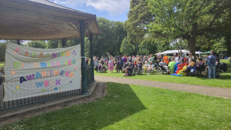 People gathered in East Park on a sunny day. The sign says Learning disabilities awareness week.