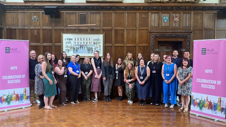 The social workers and staff are stood smiling by banners which say ASYE celebration of success.