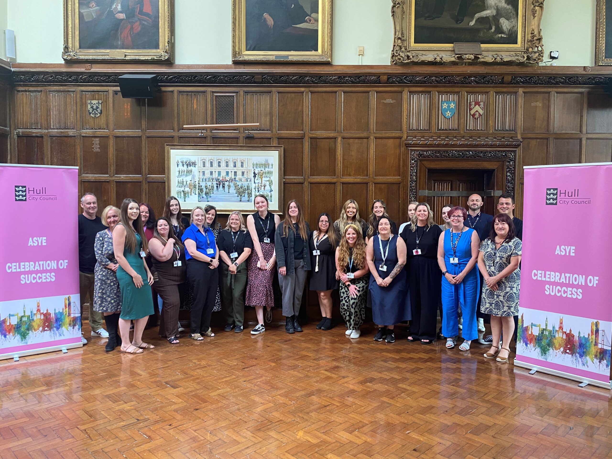 The social workers and staff are stood smiling by banners which say ASYE celebration of success.
