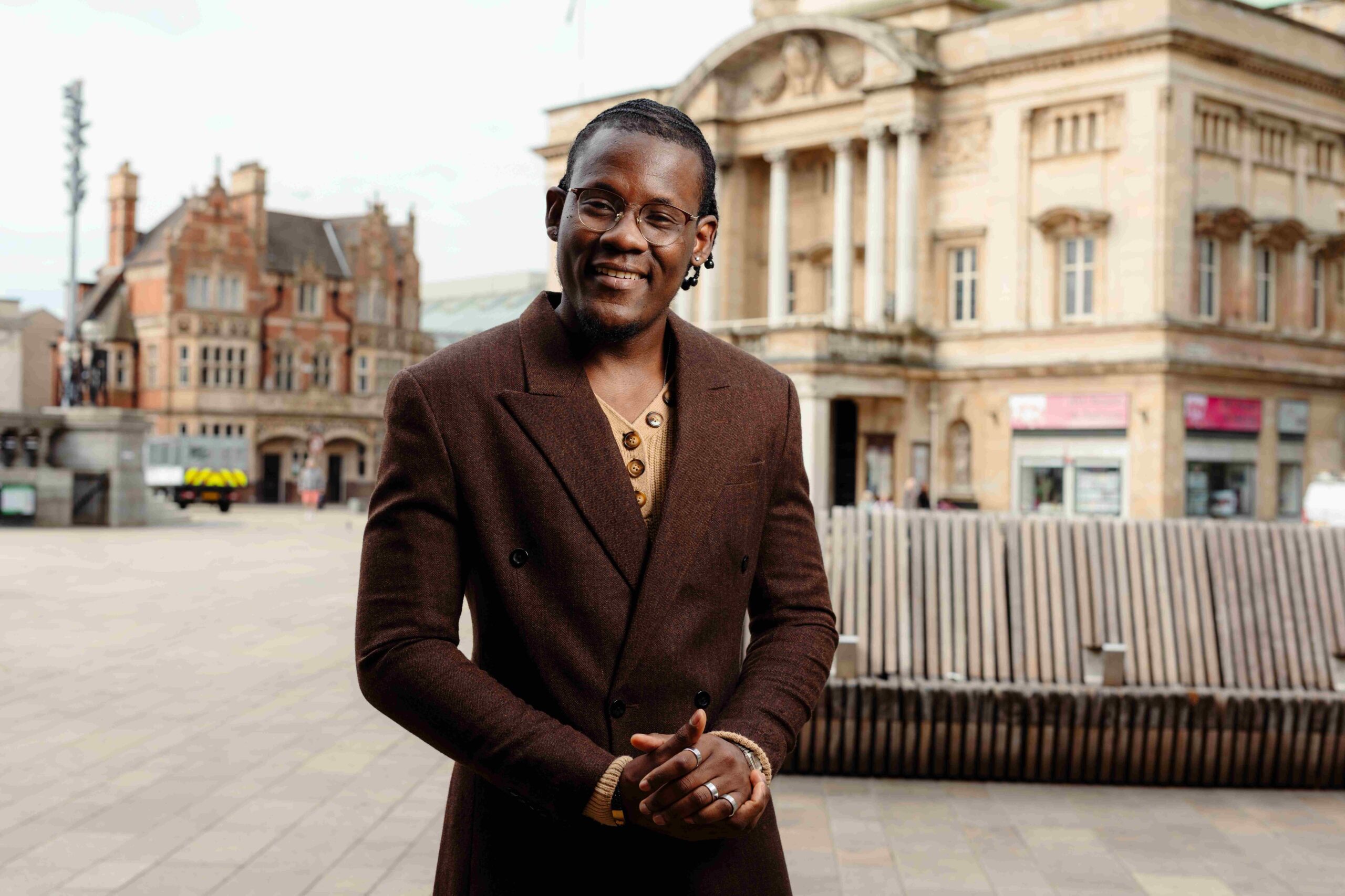 A man in a brown suit stands in the foreground with Hull City Hall behind him