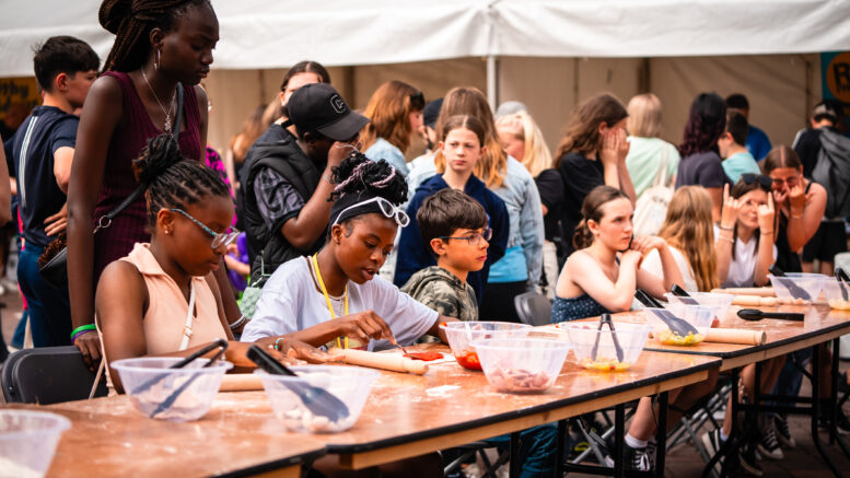In an image taken at last year's event, children and young people sit at a trestle table doing a craft activity. The background is bustling with more people