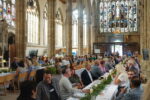 A picture from the event. A number of people sit at long trsetle tables. In the background are the ornate pillars and stained glass windows of Hull Minster