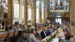 A picture from the event. A number of people sit at long trsetle tables. In the background are the ornate pillars and stained glass windows of Hull Minster