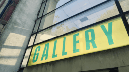 An entrance to a building with glass windows and 'gallery' written across it in green text with a yellow background