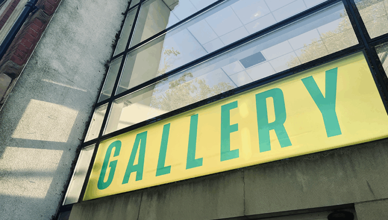 An entrance to a building with glass windows and 'gallery' written across it in green text with a yellow background
