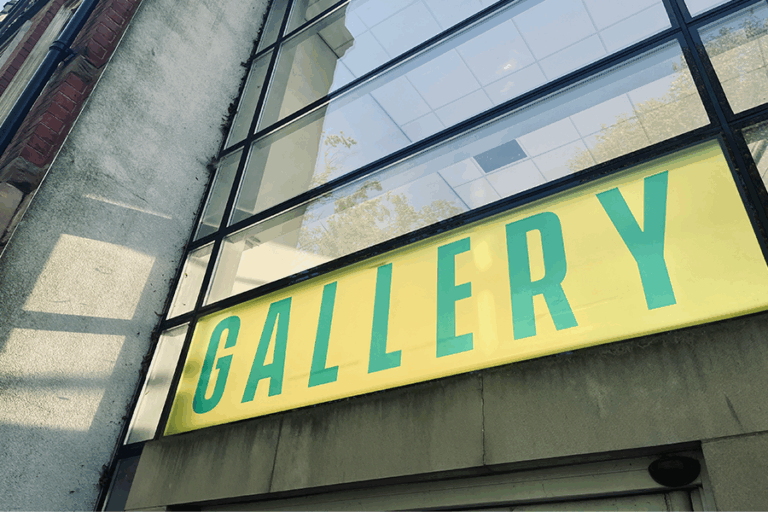 An entrance to a building with glass windows and 'gallery' written across it in green text with a yellow background