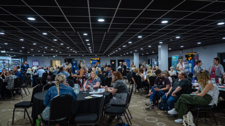 A large room with round tables and people sat around them chatting