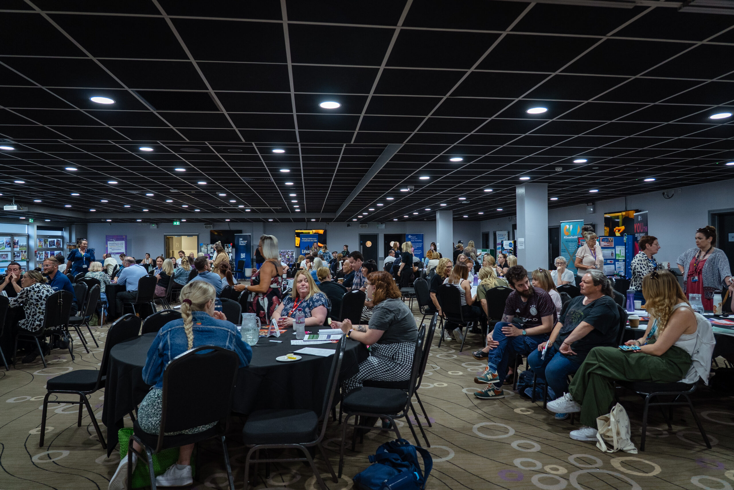 A large room with round tables and people sat around them chatting