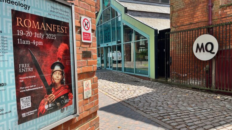 A poster form Romanfest in on an exterior wall in the foreground with the entrance to the Museums Quarter in the background
