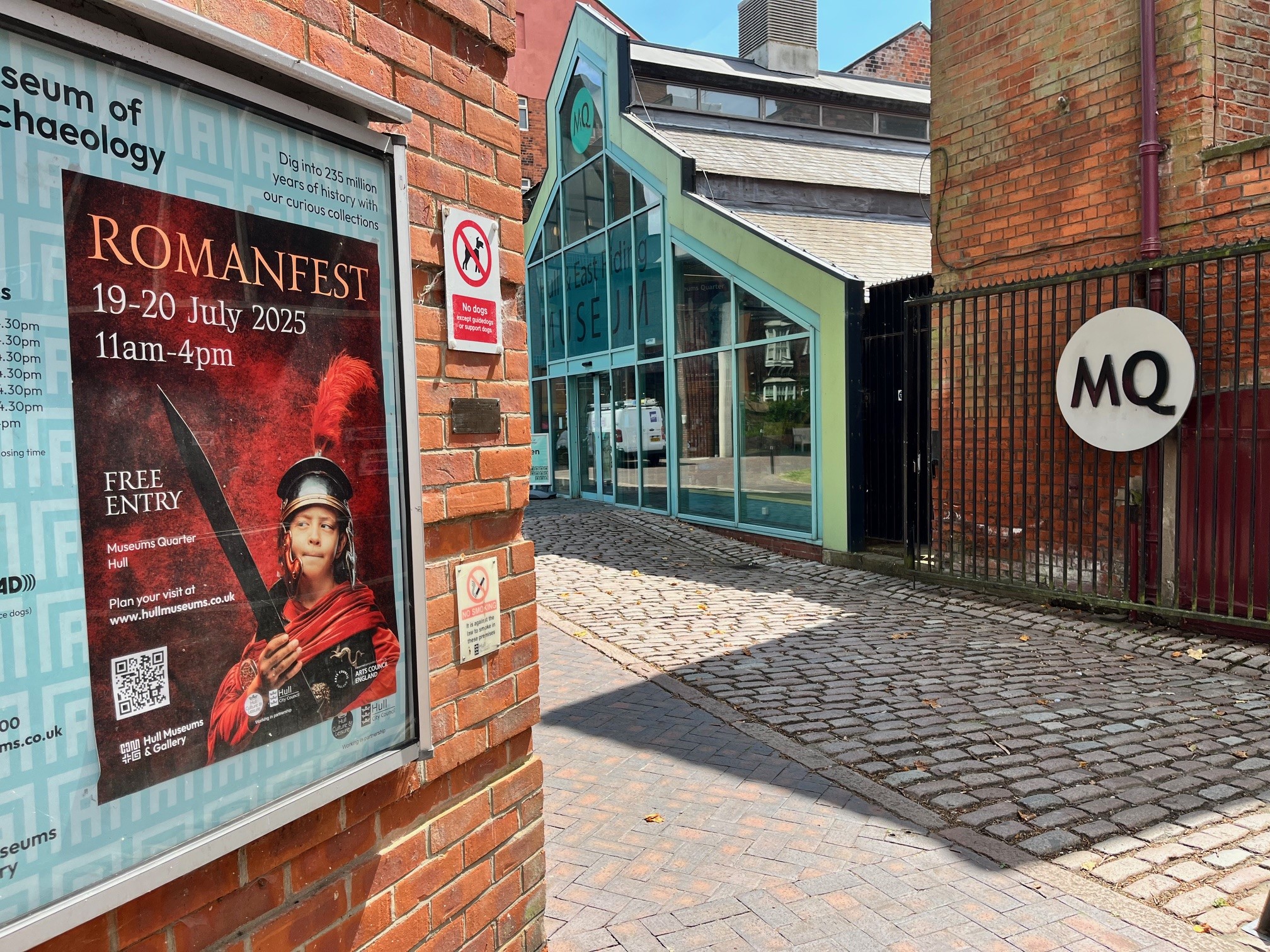 A poster form Romanfest in on an exterior wall in the foreground with the entrance to the Museums Quarter in the background