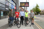 Councillor Mark Ieronimo, cabinet portfolio holder for transport and infrastructure at Hull City Council, with members of Hull’s Cycle Forum in front of a VMS sign displaying a message from the 'Share the Road' campaign.