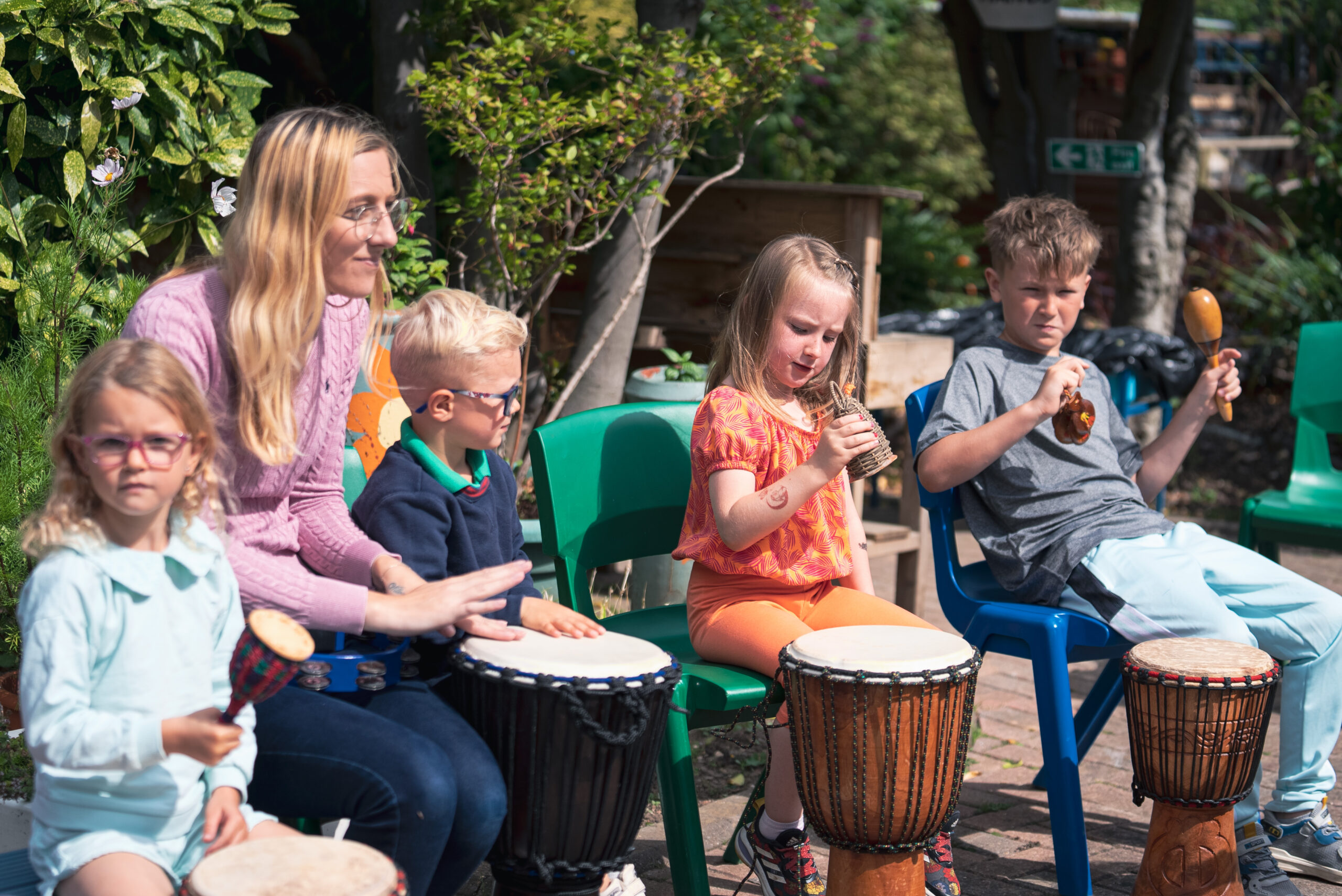 A teacher leads children in an outdoor drumming session in the sun