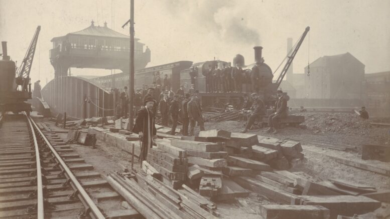 A black and white photograph of a railway with workers and a train