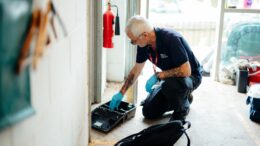 a man crouches down to bait a trap to catch pests. He wears a council uniform and protective gloves.