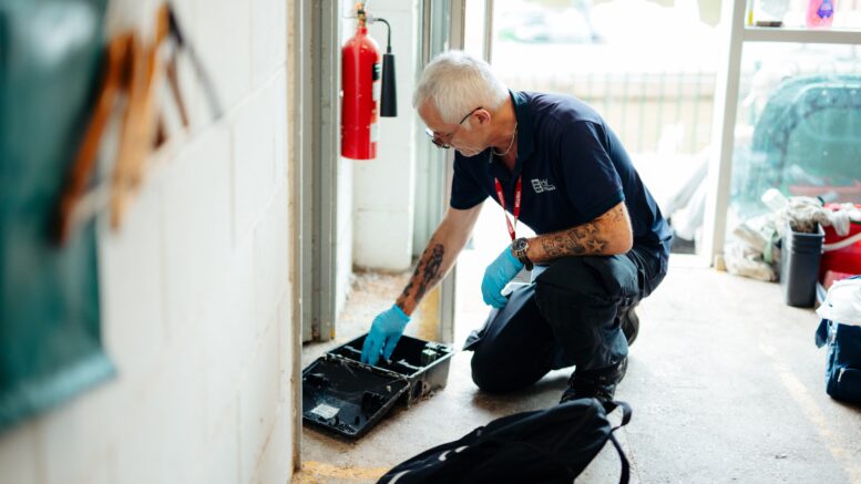a man crouches down to bait a trap to catch pests. He wears a council uniform and protective gloves.