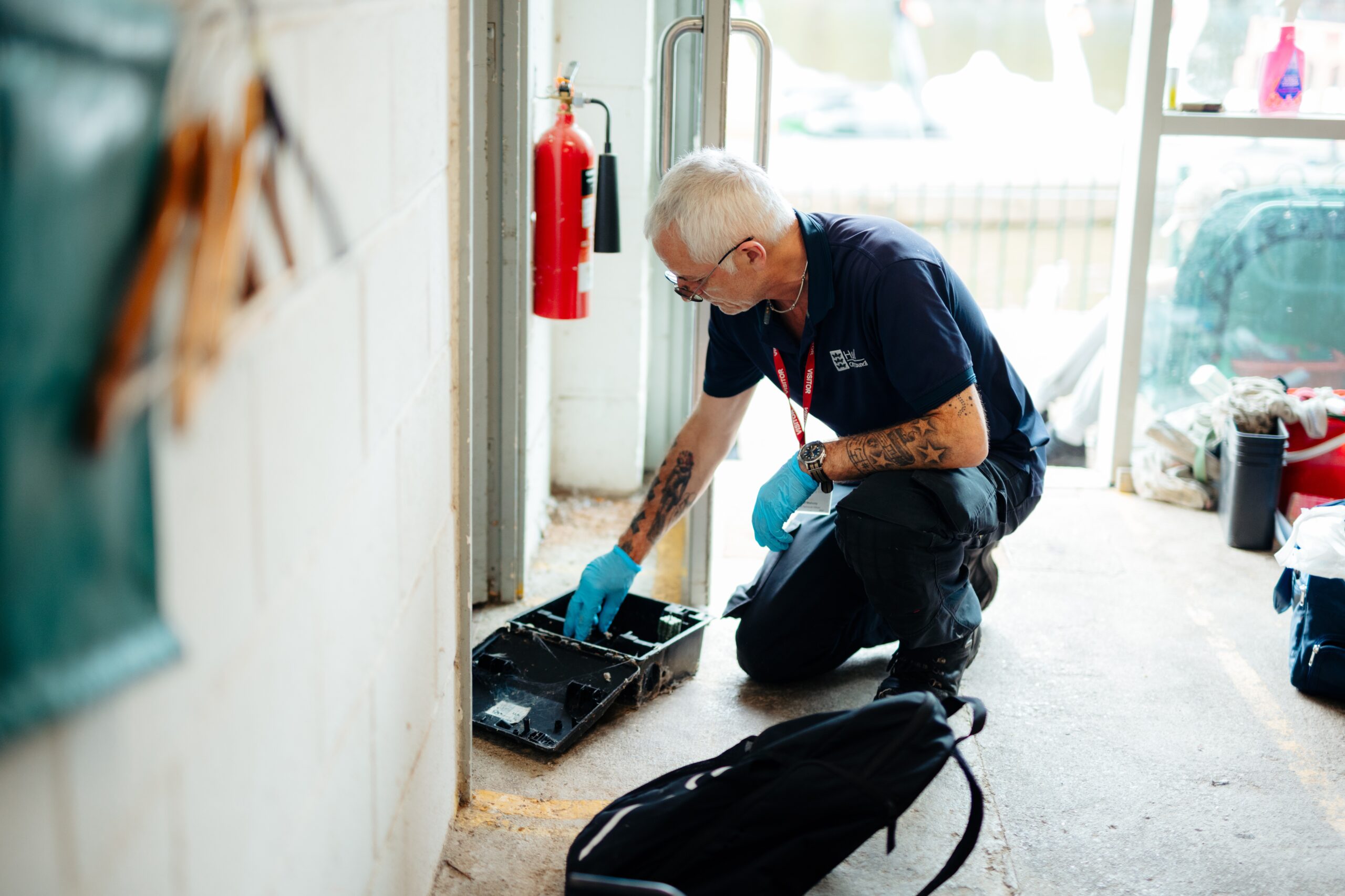 a man crouches down to bait a trap to catch pests. He wears a council uniform and protective gloves.