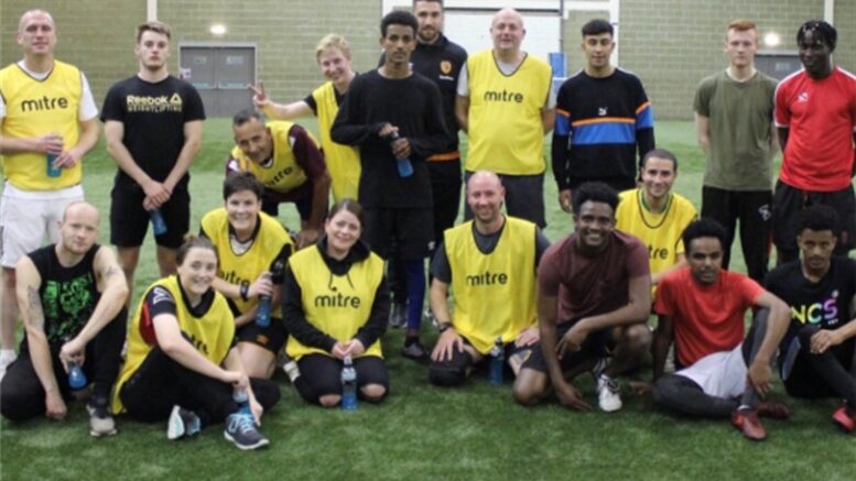 A group of people of various ages on an indoor football pitch pose together - some in yellow bibs.