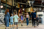 A man with 3 children walk though a museum street towards a woman with 2 children
