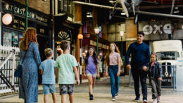 A man with 3 children walk though a museum street towards a woman with 2 children