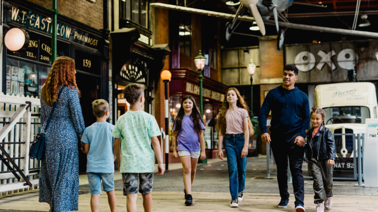 A man with 3 children walk though a museum street towards a woman with 2 children