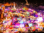 An aerial view of a fairground at night with thousands of bright lights