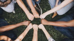 an image of a number of people making a fist and placing their hands together to form a circle. Only their arms and hands can be seen