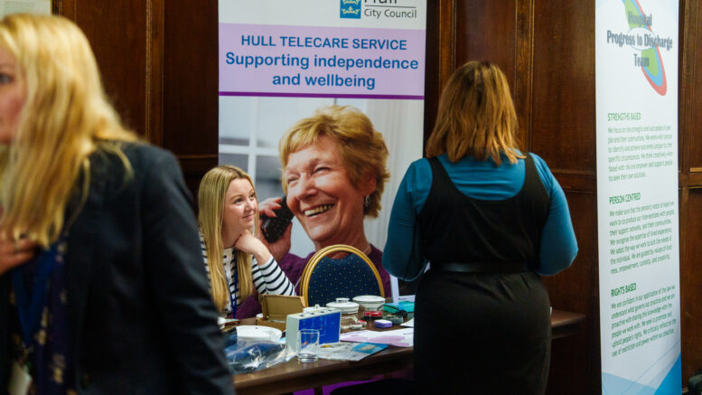 A woman sits listening to someone at an adult social care event