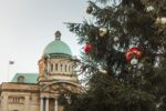 An old building with green roof in background and part of a large christmas tree with red and gold baubles in foreground