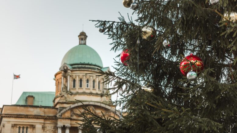 An old building with green roof in background and part of a large christmas tree with red and gold baubles in foreground