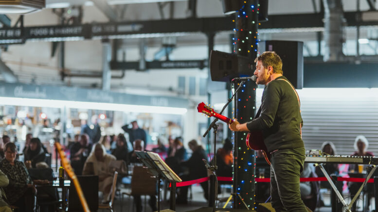 A male singer with a guitar is performing on an indoor stage to a crowd