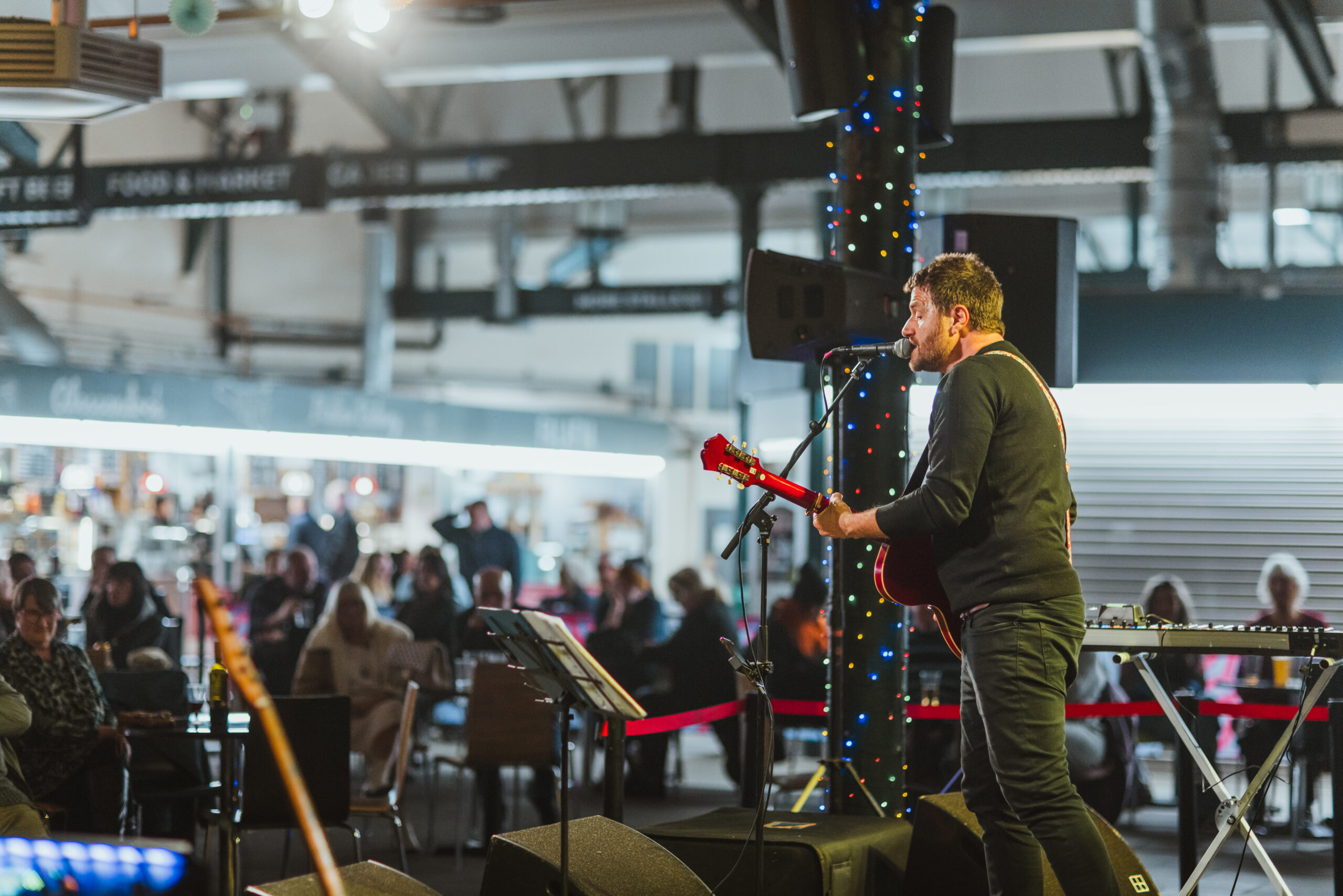 A male singer with a guitar is performing on an indoor stage to a crowd