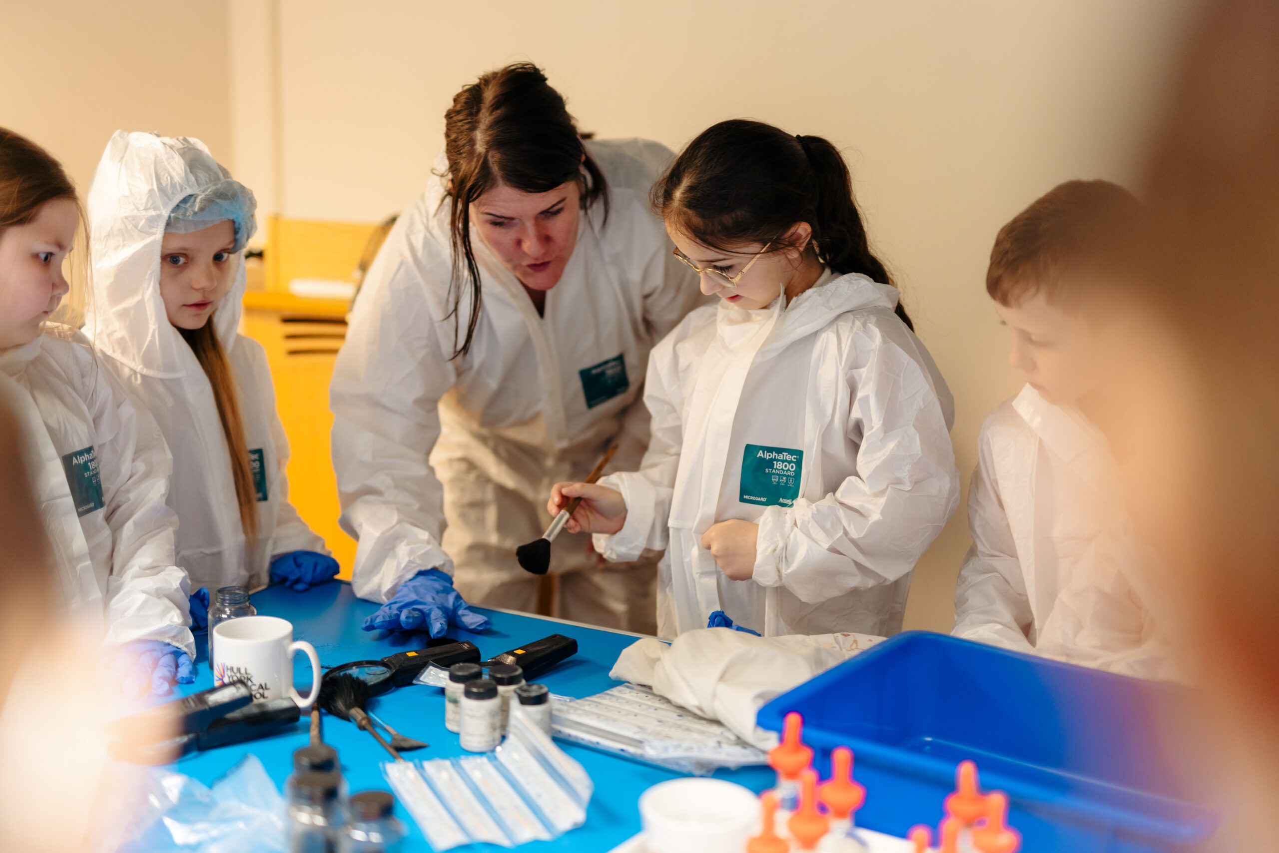 An image of a woman and children in science lab coats doing a science experiment at a table