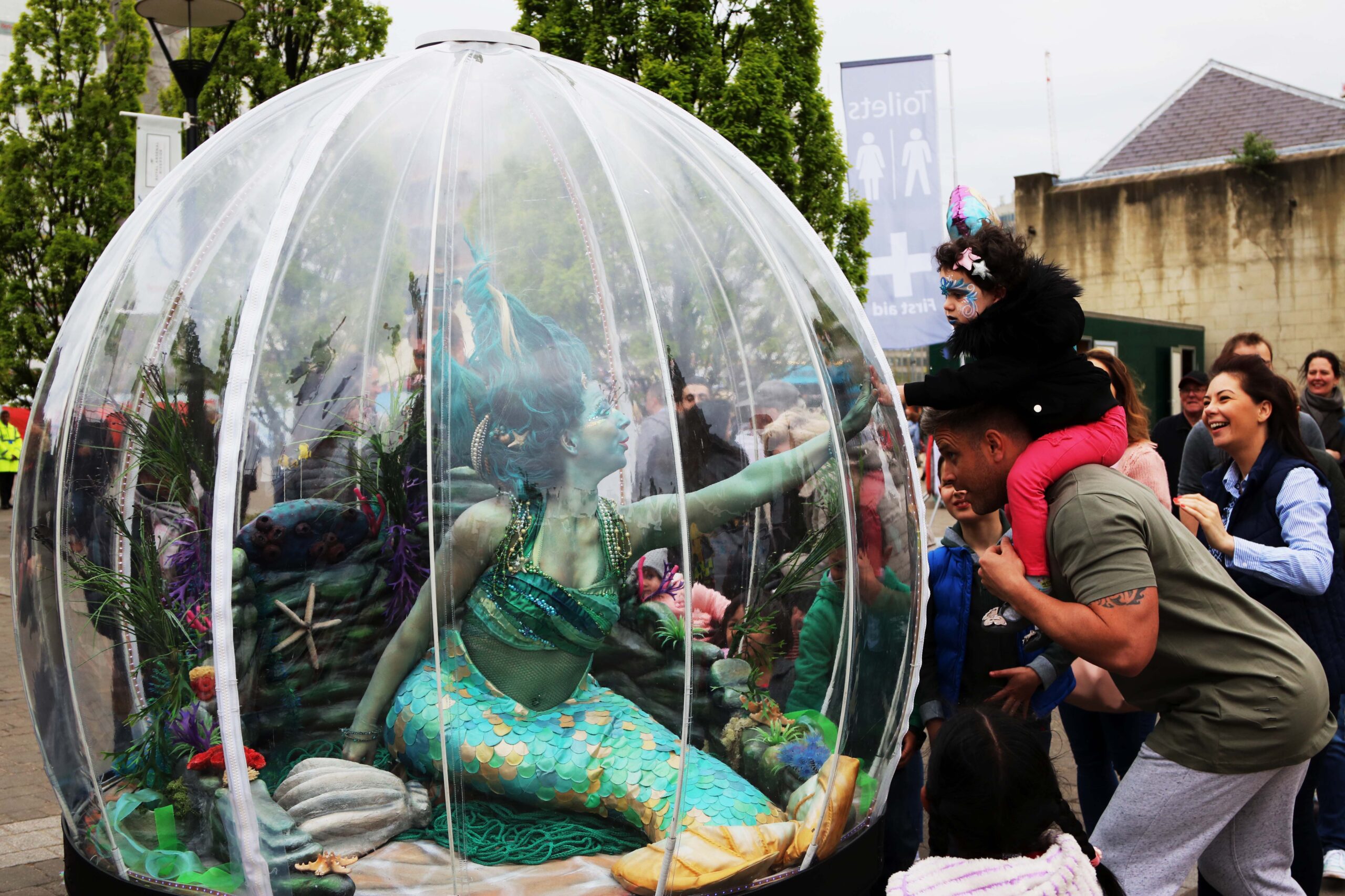 A large snowglobe with a green mermaid character inside, with crowds of people looking in