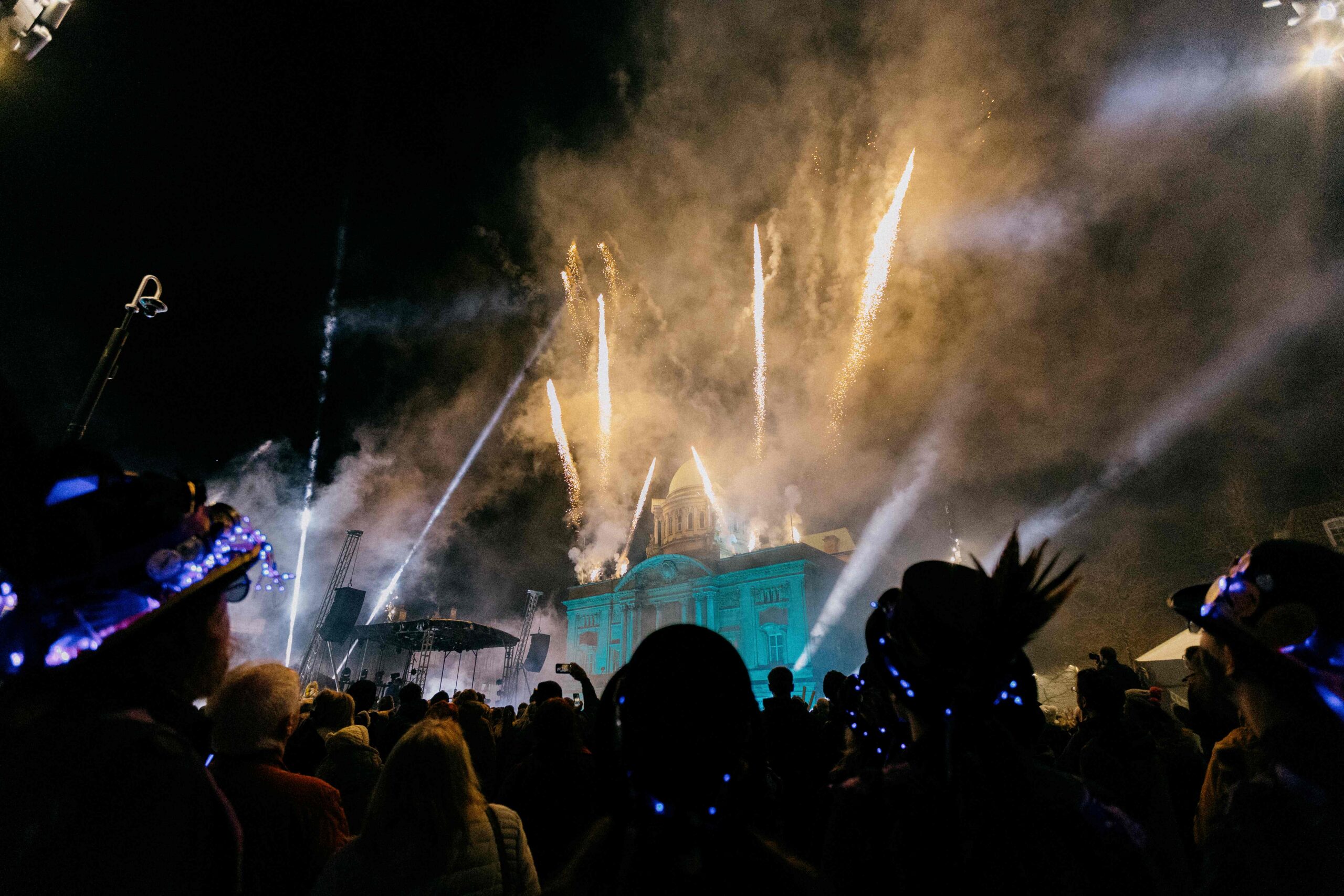 A night shot of fireworks and lights int sky above a civic building with crowds of people below