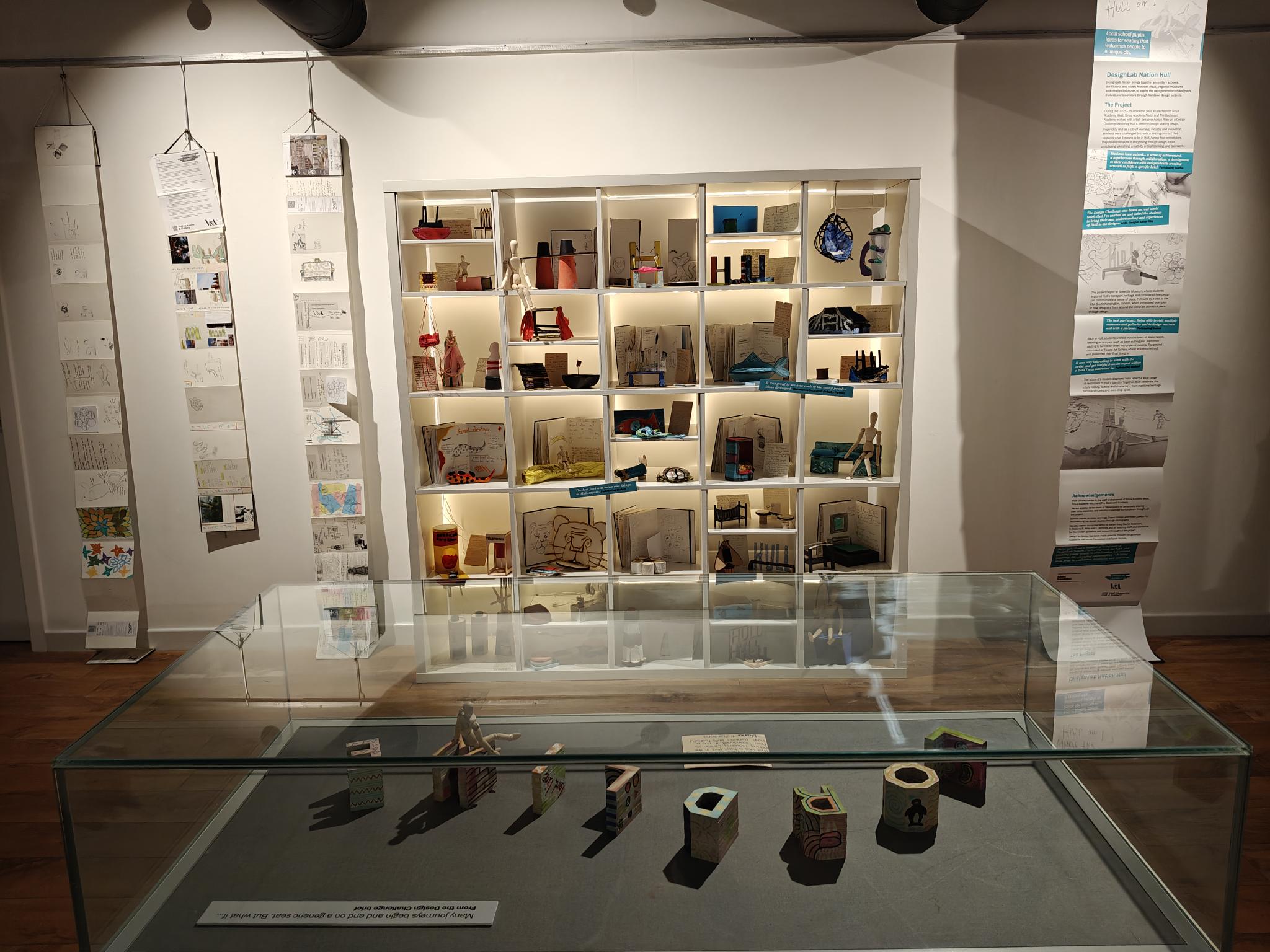 An image of a room with white walls and paper hanging from the ceiling. and a set of open shelving with models of seating on it