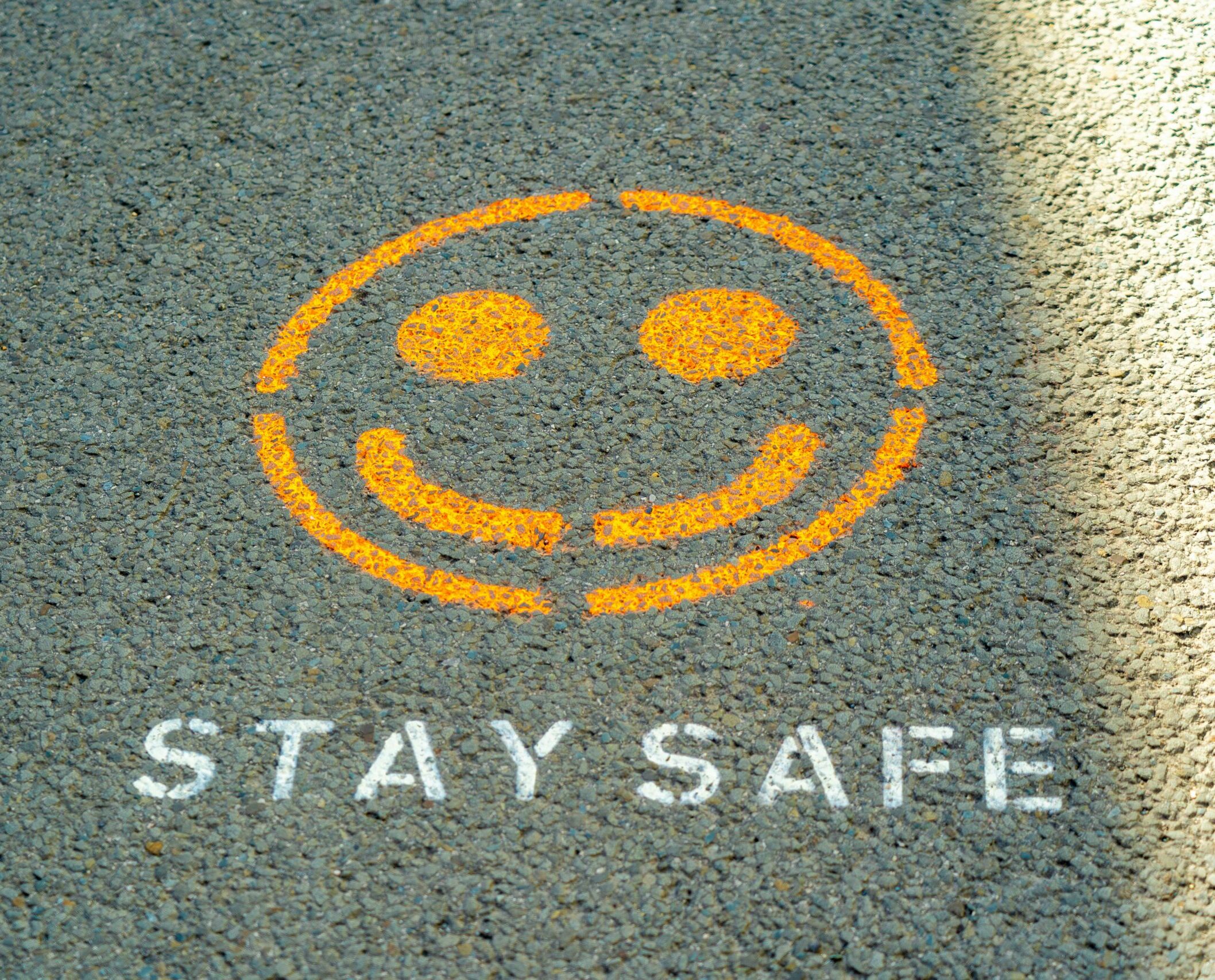 An image of a smiley face painted on the ground with the words 'stay safe' beneath